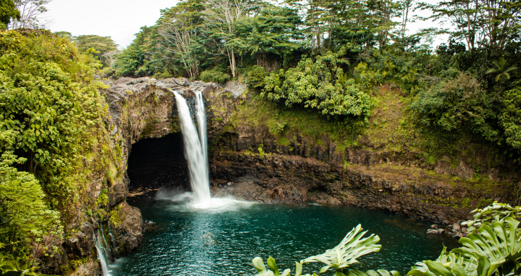 Waterfall at a distance surrounded with greenery, as we discover the Majestic Big Island Waterfalls.