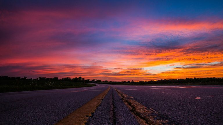A highway stretching into the distance, with the warm and beautiful colors of a sunset bathing the sky and the surrounding landscape.
