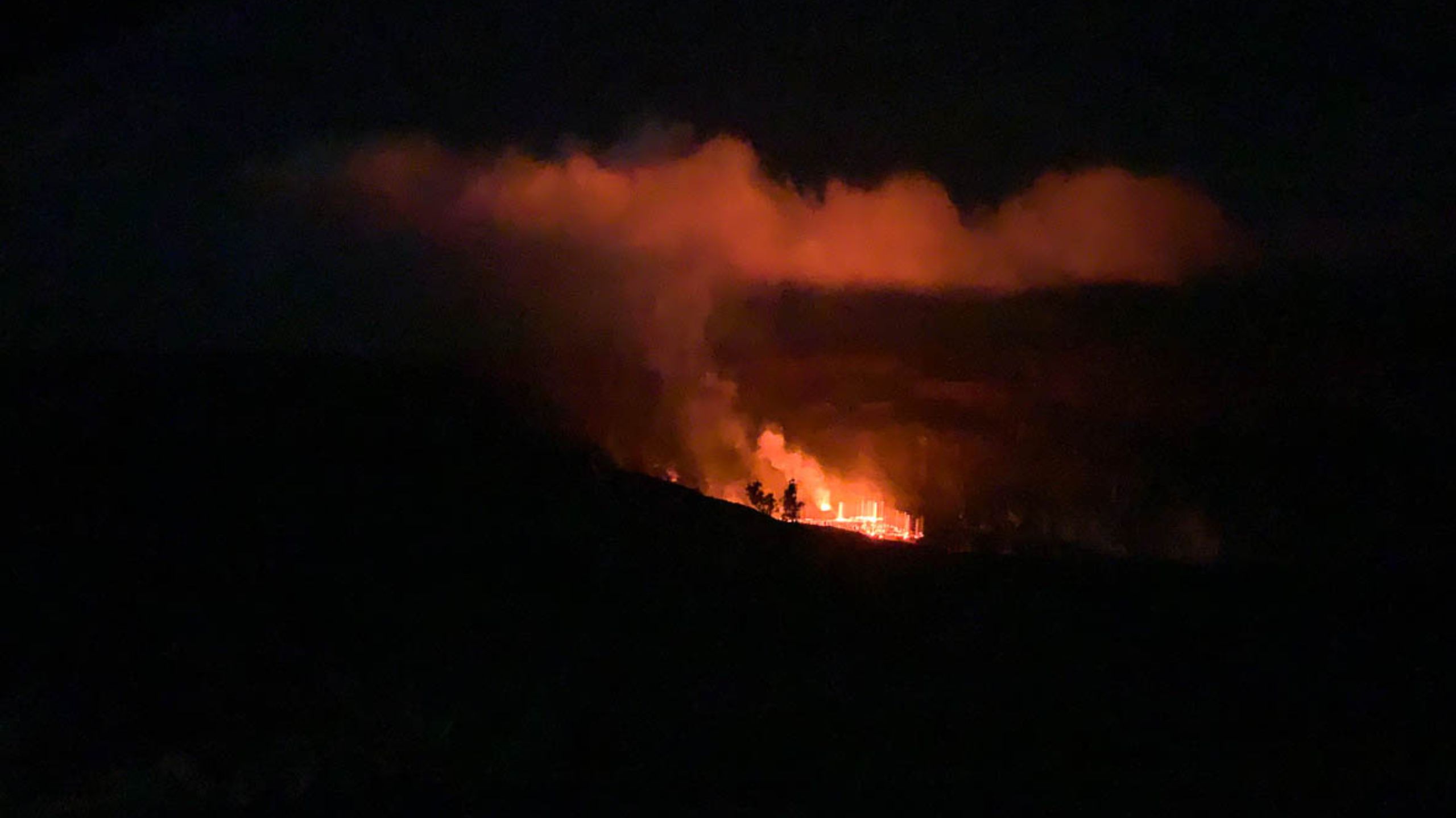 bubbling lava at night with smoke rising at a distance