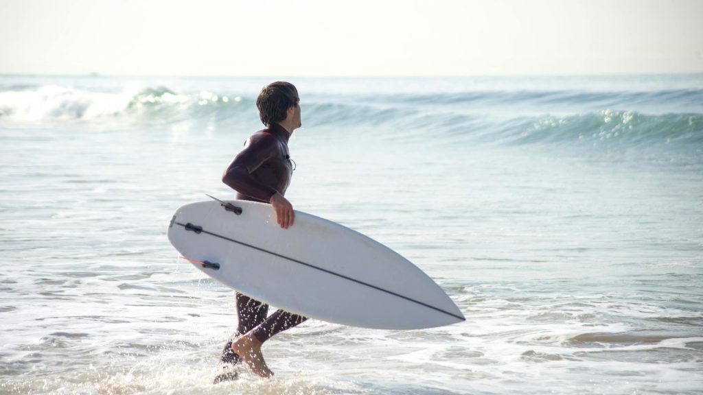 Man entering the sea while holding a surfboard