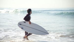 Man entering the sea while holding a surfboard